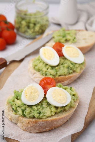 Delicious sandwiches with guacamole, eggs and tomatoes on parchment paper, closeup