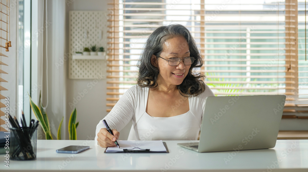 Portrait of middle age woman sitting at cozy home interior working on laptop with a happy face.