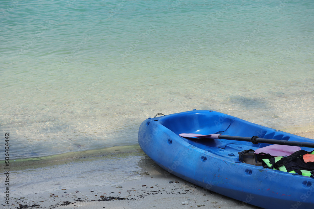 Blue Kayak on the tropical white sand beach with sea waves. Clear water of sea waves on the beautiful beach. Scenic relaxing scenery Blue Kayak on the tropical white sand beach with sea waves. Clear water of sea waves on the beautiful beach. Scenic relaxing scenery