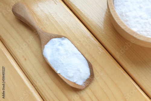 Top view of baking soda (sodium bicarbonate) with wooden spoon on wooden table. Home cleaning concept.