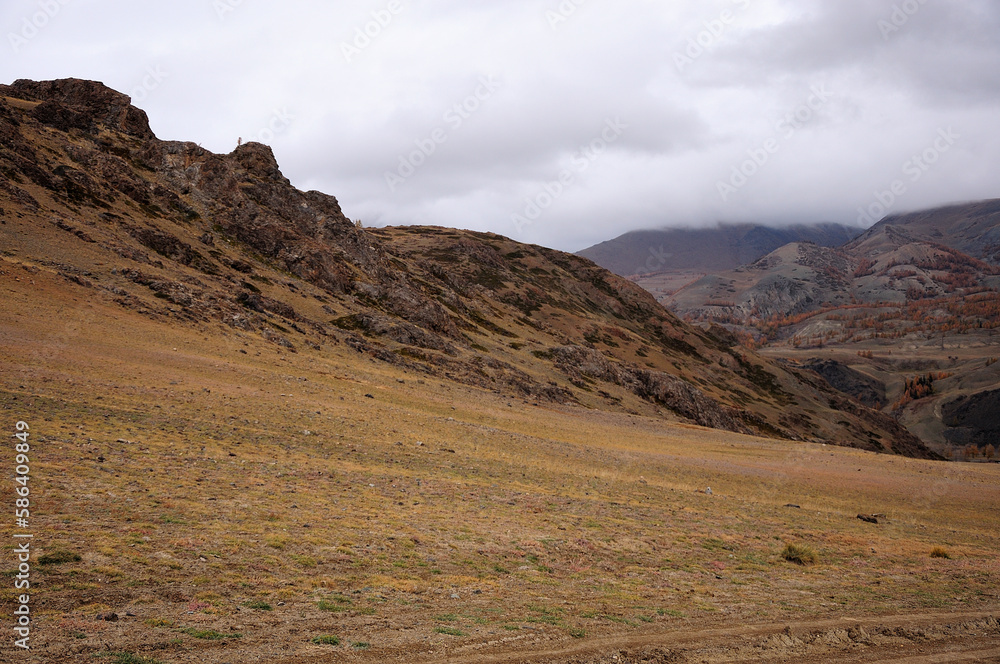 The gentle slope of a high rocky hill under thunderclouds in the autumn dried steppe.