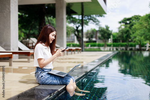 A woman using a smartphone during a vacation near the swimming pool in a resort hotel