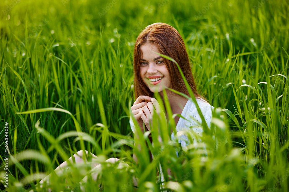 portrait of a beautiful, happy woman sitting in the grass in a light dress and smiling at the camera portrait of a beautiful, happy woman sitting in the grass in a light dress and smiling at the camera