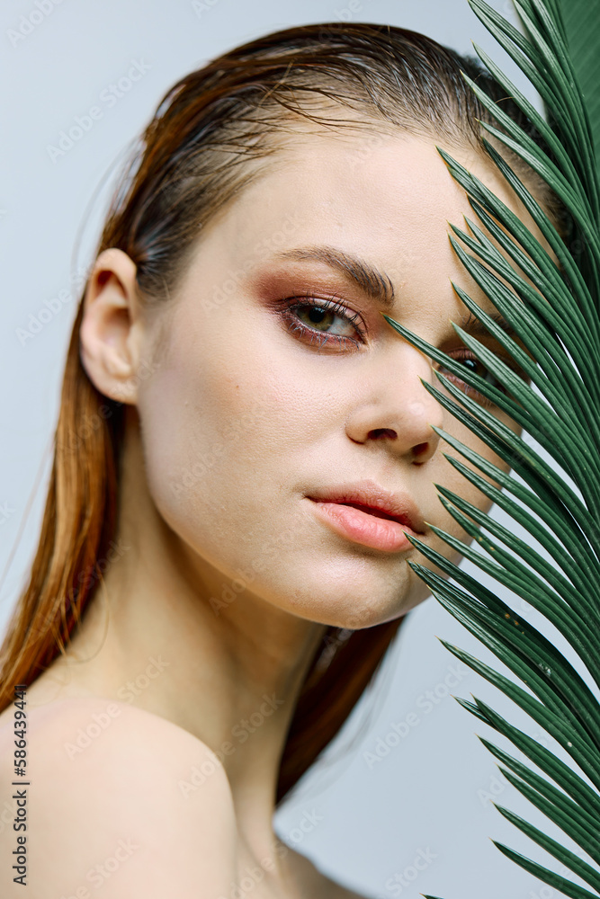 a close beauty portrait of a beautiful woman standing holding a tropical palm leaf in her hand, bringing it to her face. Vertical photo without retouching a close beauty portrait of a beautiful woman standing holding a tropical palm leaf in her hand, bringing it to her face. Vertical photo without retouching