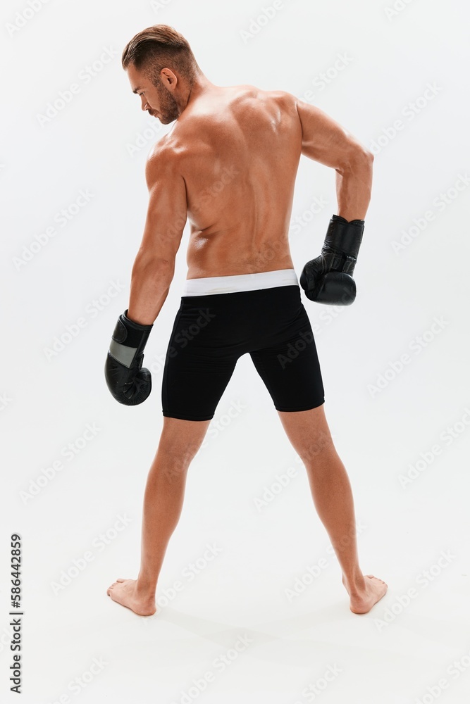 Man athletic bodybuilder poses in boxing gloves with nude torso abs in full-length background, boxing and martial arts. Advertising, sports, active lifestyle, competition, challenge concept. 