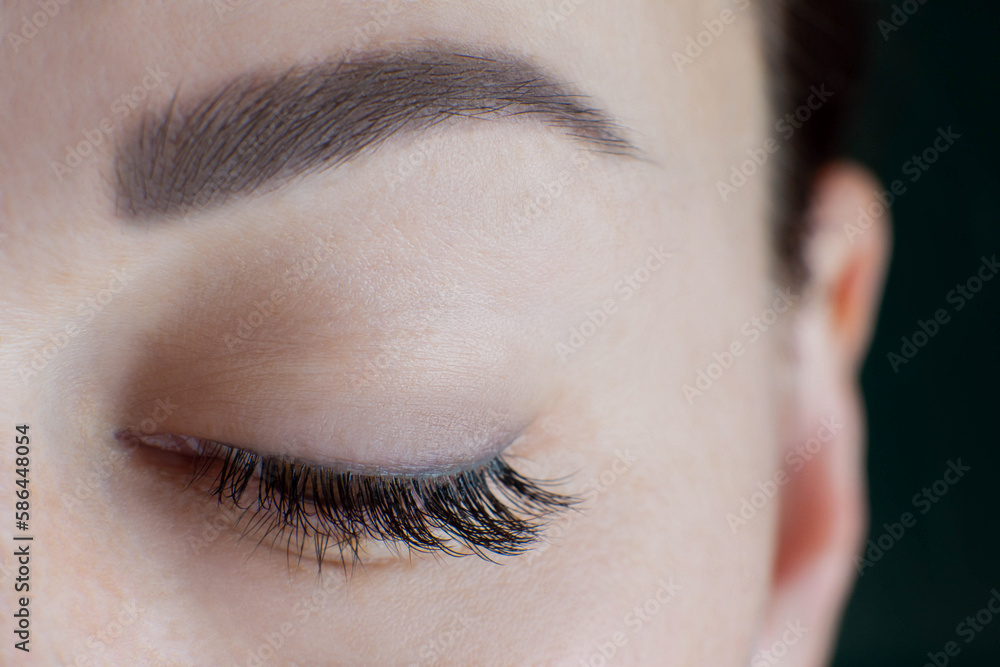 Close-up of brown eye with beautiful long eyelashes, black eyeliner, ideal skin, eyebrow of unrecognizable young woman looking down. Macro. Eyelash extension, beauty procedures, make-up. Soft focus.