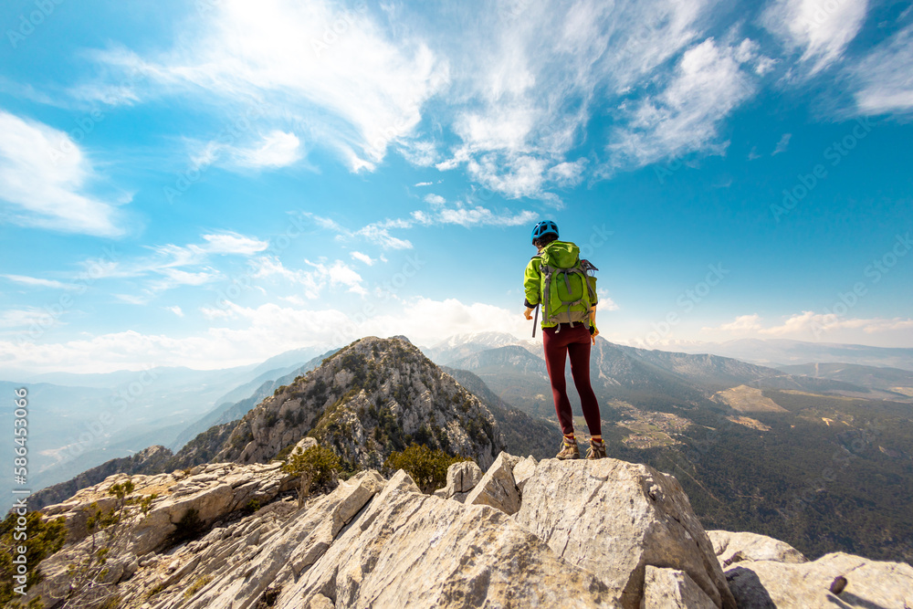 Woman climber with backpack and helmet enjoys amazing mountain view before climbing on a summer day. adventure and mountaineering concept. hiking with a backpack in the mountains.