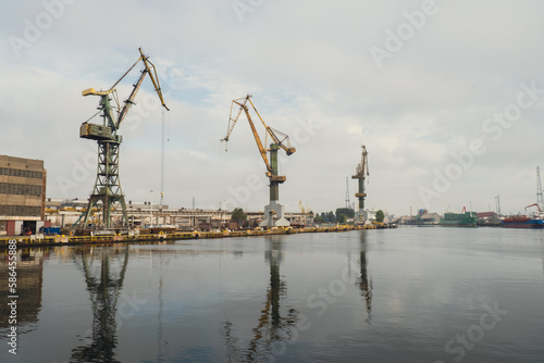 Motlawa river to Baltic Sea. Coal mine, polluting environment by the river POV from ferry swimming on river canal. Industrial building at the Gdansk Shipyard. Prefabrication workshop and heavy cranes