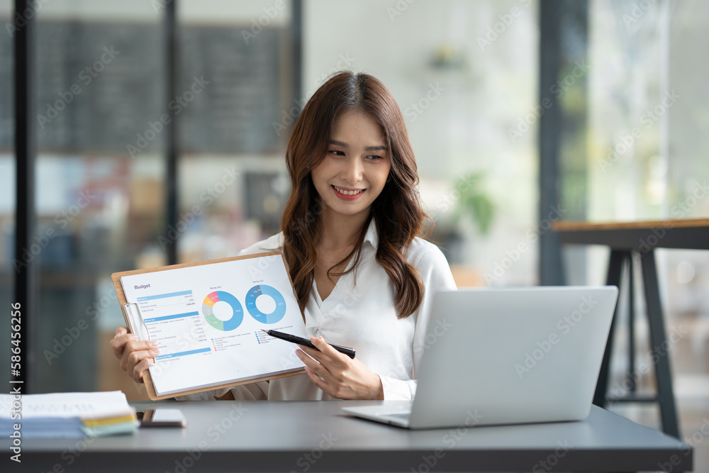 Asian businesswoman sitting in an office looking with graph detail on laptop computer Chart of real estate business growth data in the office. Asian businesswoman sitting in an office looking with graph detail on laptop computer Chart of real estate business growth data in the office.