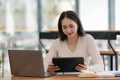 An Asian businesswoman using a digital tablet while sitting at a work desk in an office