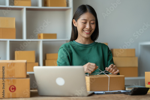Asian businesswomen tie boxes with ropes in preparation for delivery to customers. Young Asian small business owners use computers. Shipping boxes online market SME e-commerce telemarketing concept. © crizzystudio