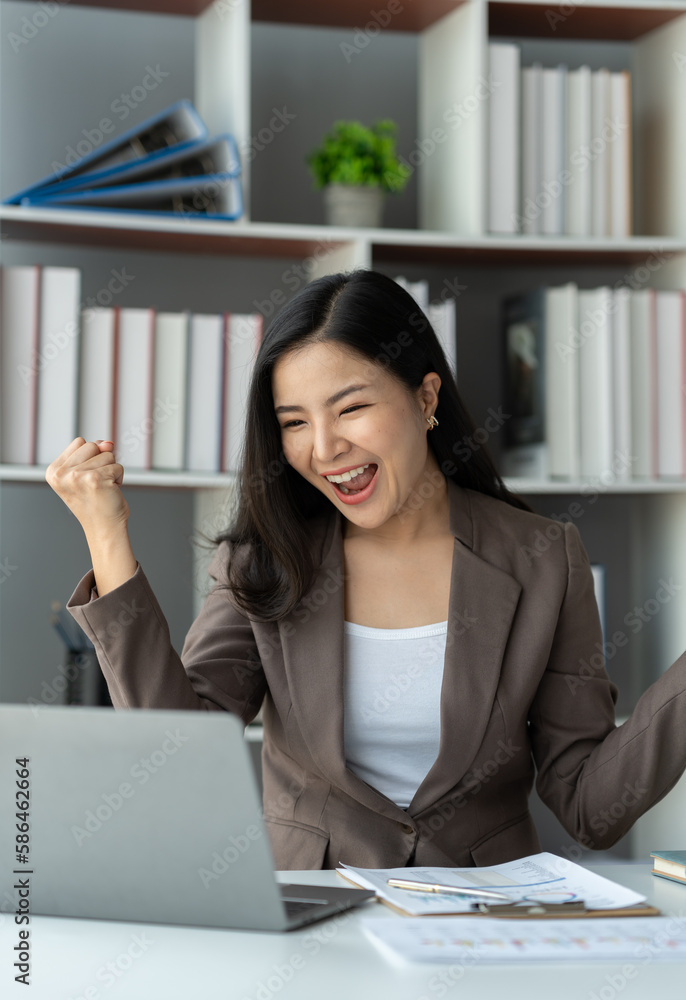 Asian businesswoman, investor showing a happy expression to know the results of financial approval Revenue that has been agreed in the business of real estate projects on a laptop computer in office. Asian businesswoman, investor showing a happy expression to know the results of financial approval Revenue that has been agreed in the business of real estate projects on a laptop computer in office.