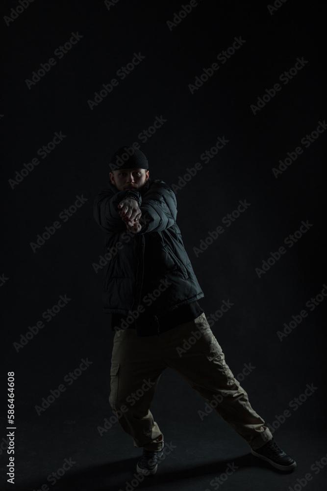 Fashionable professional dancer man with a hat in a down jacket is dancing in the dark. Dancing guy silhouette Fashionable professional dancer man with a hat in a down jacket is dancing in the dark. Dancing guy silhouette