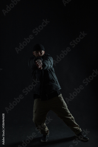 Fashionable professional dancer man with a hat in a down jacket is dancing in the dark. Dancing guy silhouette