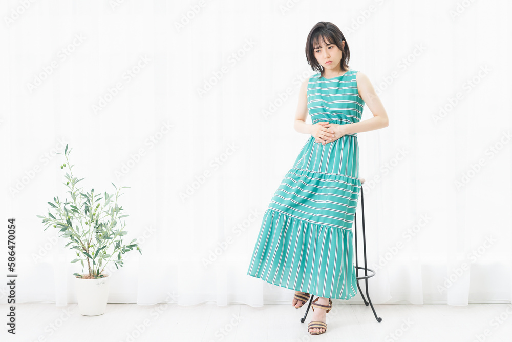 窓際で、お腹に手を当てている若い女性