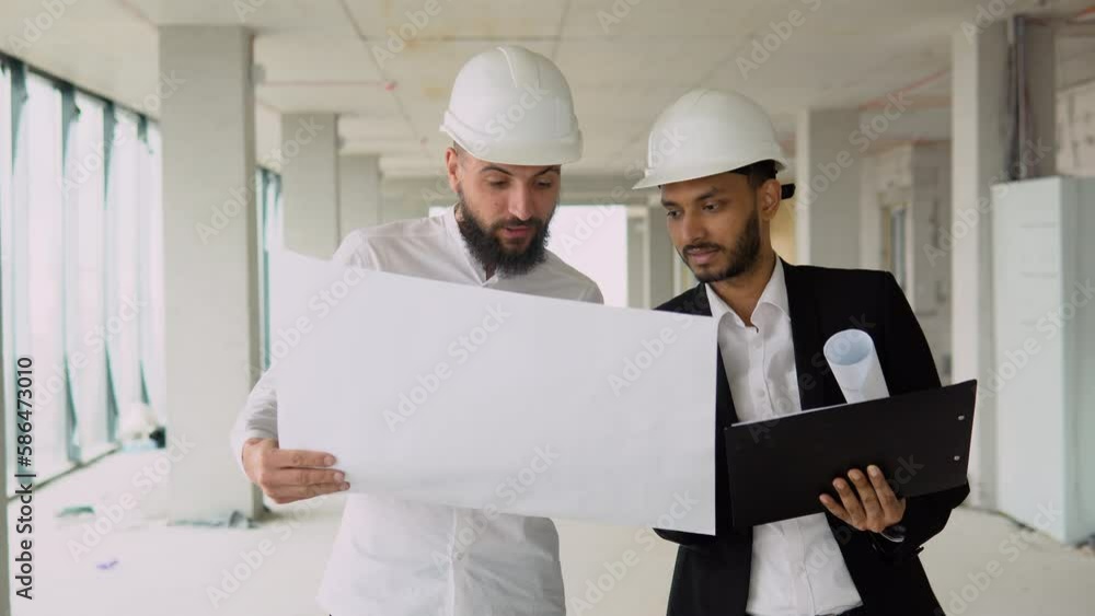 Indian architect and arabian supervisor meeting at construction site. Multiethnic engineers discussing on plan. Two construction workers working together while visiting a new building Indian architect and arabian supervisor meeting at construction site. Multiethnic engineers discussing on plan. Two construction workers working together while visiting a new building