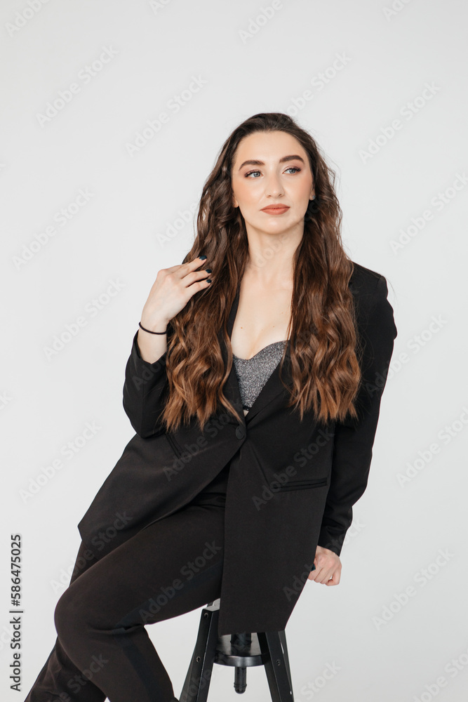 young businesswoman with long curly hair in a black suit sitting on a white background young businesswoman with long curly hair in a black suit sitting on a white background