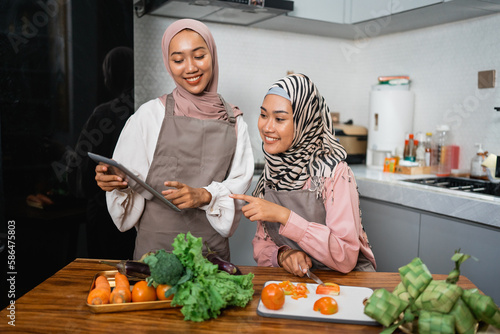 two friend with hijab looking tablet and learn to make new food menu in the kitchen. cooking recipe