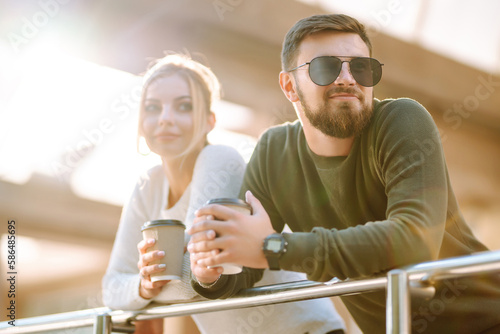 Young couple having fun talking, drinking coffee and using the phone while walking in the morning city. Relaxation, youth, love, lifestyle, selfie, blogging.
