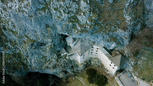 Descending, Tilting Up Revealing Shot Of Historic Medieval Predjama Castle, Built Into Mouth Of a Cave, Under The Cliff. Popular Tourist Attraction Surrounded With Cliff, Stones, Rocks, Caves, Birds.