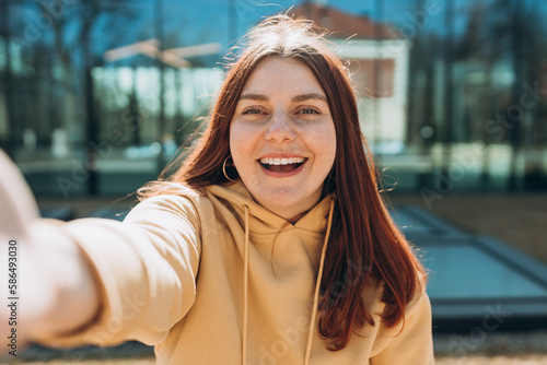 Young happy woman is making selfie on a camera on city street. Urban life concept. Girl talking on a video call with phone outdoor. photo