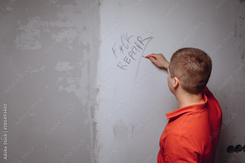 A young man standing with his back writes abusive words on an empty white wall with a graphite pencil. A young man standing with his back writes abusive words on an empty white wall with a graphite pencil.