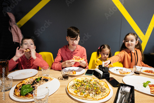 Four kids eating italian pizza in pizzeria. Children eat at cafe.