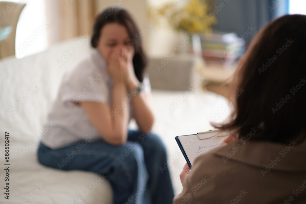 woman finds solace in the confidence and support of her therapist during a counseling session. The psychologist takes notes to ensure that the therapy remains confidential woman finds solace in the confidence and support of her therapist during a counseling session. The psychologist takes notes to ensure that the therapy remains confidential
