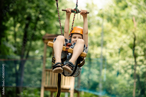 A young boy is hanging on the line in the rope park. Sports entertainment for a child, active rest.