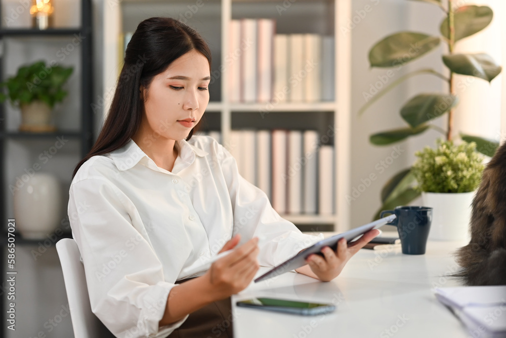 Modern millennial woman using digital tablet, working from home in cozy interior