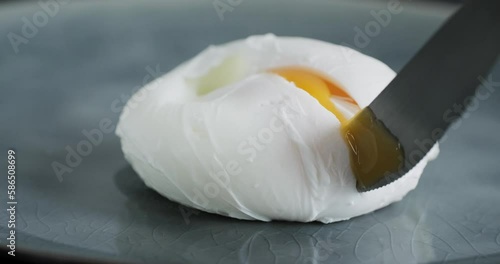 Cutting a poached egg with runny egg yolk with knife and fork, close up video clip, benedict egg on plate, high quality 4k video footage