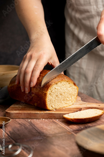 Woman cutting sourdough white loaf bread on wooden board. Homemade healthy cooking concept.