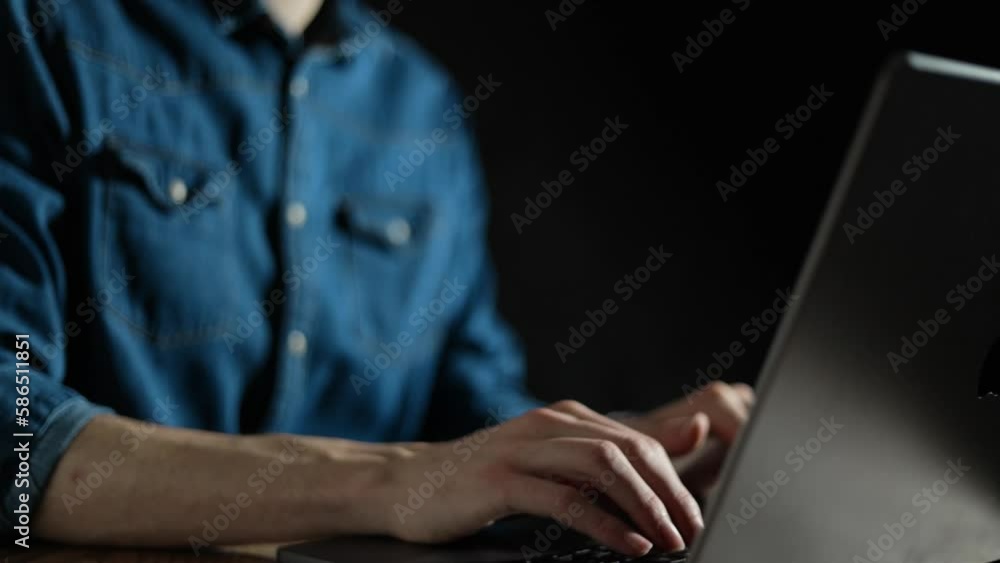 Man typing on his laptop keyboard in a dark studio place at night. Businessman working and doing research on his computer late at night video. Modern pc and office black background Man typing on his laptop keyboard in a dark studio place at night. Businessman working and doing research on his computer late at night video. Modern pc and office black background