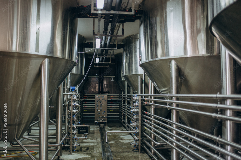 Obraz premium Row of tanks in brewery. Fermentation in brewery tanks with beer for brewing. Modern beer factory. Big steel tanks for storage. Camera view from top to bottom.