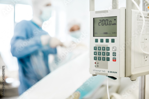 Team of Surgeons Operating in the Hospital. Man in protective costume and mask performing an operation. Cardiogram monitor at foreground. White hospital room. Concept of heart disease, physical health