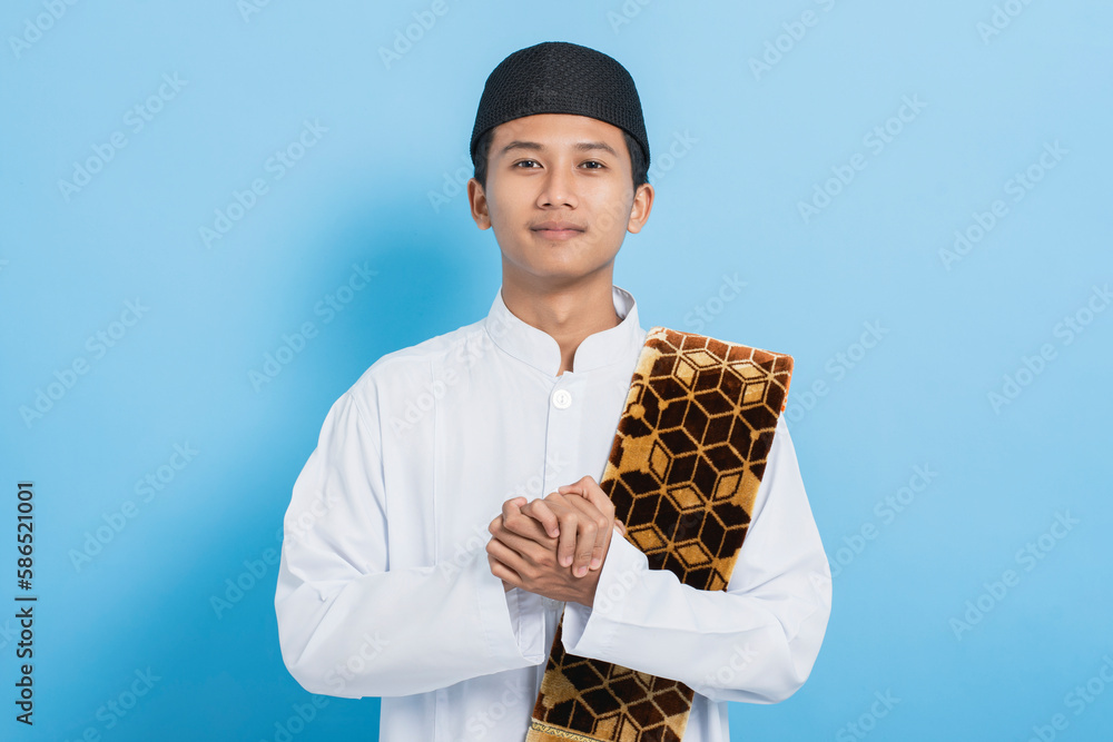 Asian muslim man carrying praying mat happy celebrate ramadan mubarak and eid al-fitr isolated on blue background Asian muslim man carrying praying mat happy celebrate ramadan mubarak and eid al-fitr isolated on blue background