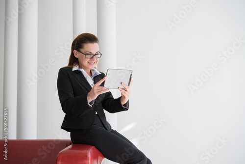 Image of young caucasioan woman in black costume wearing eyeglasses, company worker in glasses, smiling and holding digital tablet, standing over white background. Concept of success and technology. photo