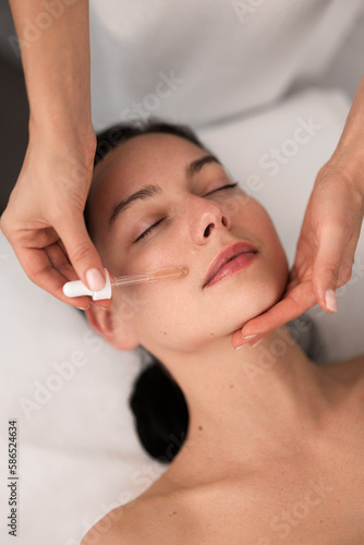 Crop beautician applying serum on clients face