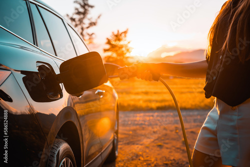 Young woman plugging in the charger in a black electric car, renewable energy concept © 24K-Production