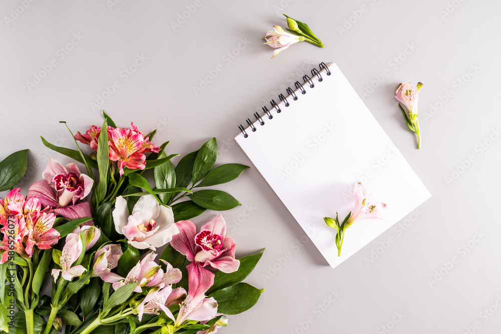 blank sheets of notebook on a black spring and a bouquet of spring flowers on a pastel background. top view. festive background.