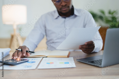 middle age man American African using calculator for calculating and laptop computer with planning working on financial document, tax, exchange, accounting and Financial advisor