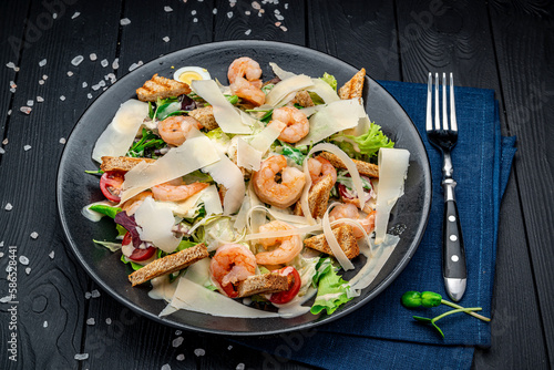 Caesar salad with grilled shrimp on a dark background, top view