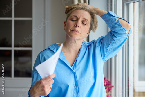 Menopausal Mature Woman Having Hot Flush At Home Cooling Herself With Letters Or Documents photo