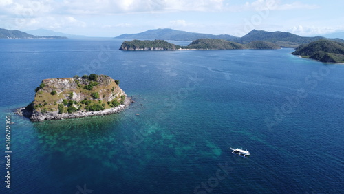 Small tropical island in the middle of the sea. Motor boat next to the island. Aerial view of an island in the ocean.