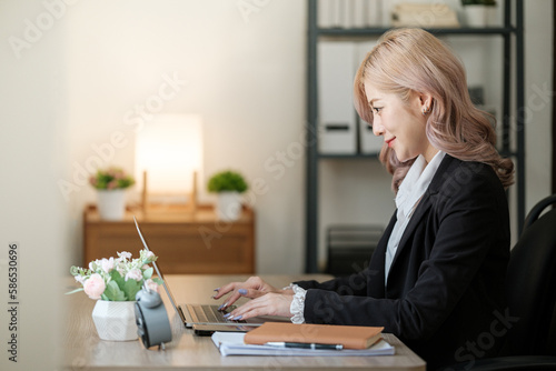 Close up on laptop in office, Asian happy beautiful businesswoman in formal suit work in workplace. Attractive female employee office worker smile.