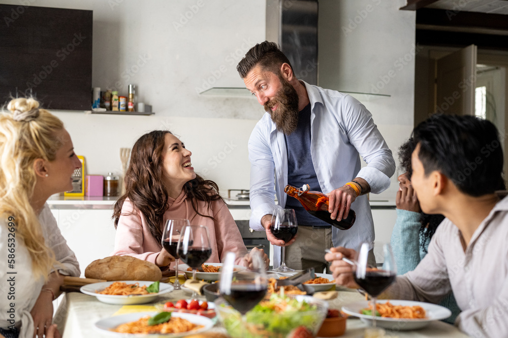 Friends gathering having Italian food together,Young bearded man pours red wine in glass to young woman