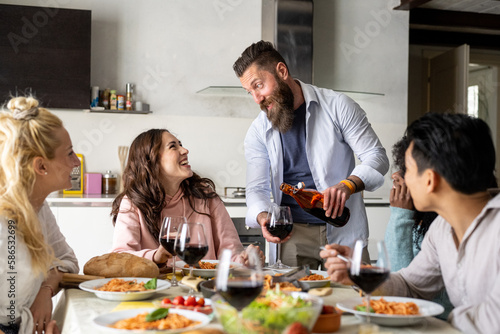 Friends gathering having Italian food together Young bearded man pours red wine in glass to young woman