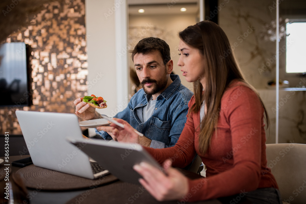 A multitasking couple at home - breakfast and work happening simultaneously. A multitasking couple at home - breakfast and work happening simultaneously.