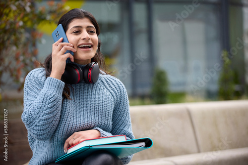 Female College Or University Student Outside Campus Building Wearing Wireless Headphones Talking On Mobile Phone photo