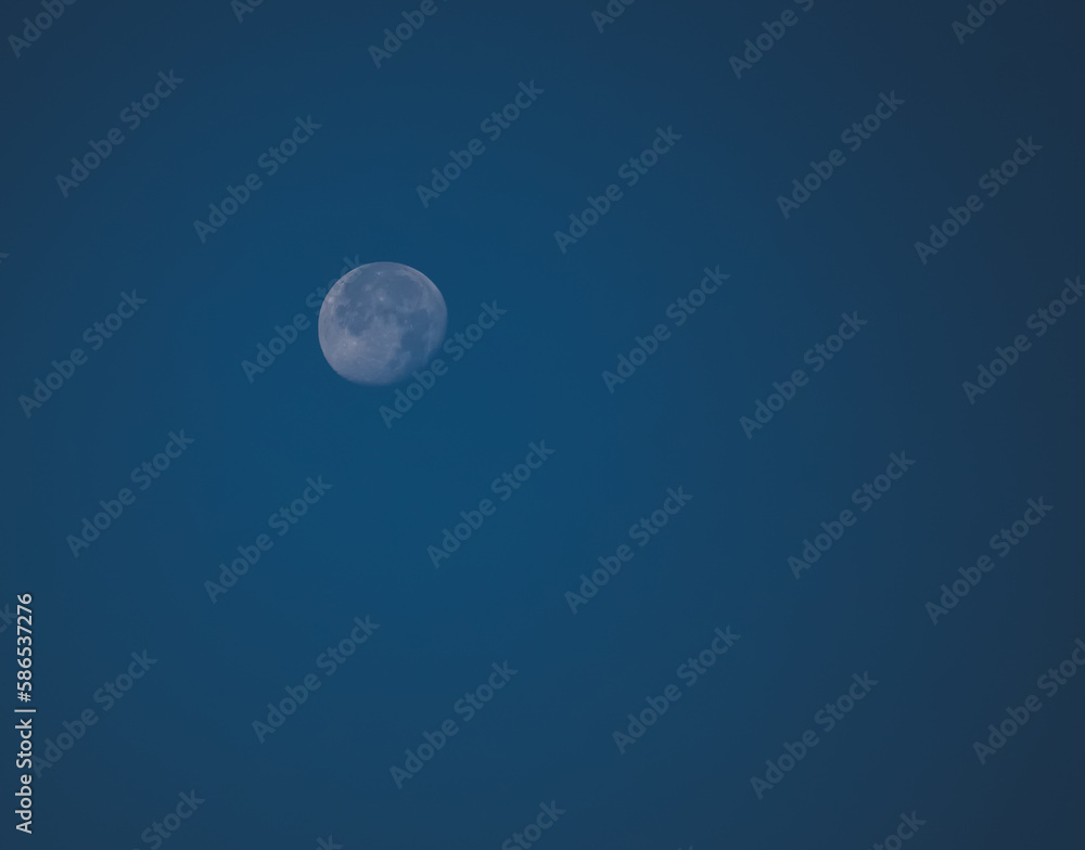 Minimalistic view of the waning moon against the blue sky, the moon is the satellite of the earth